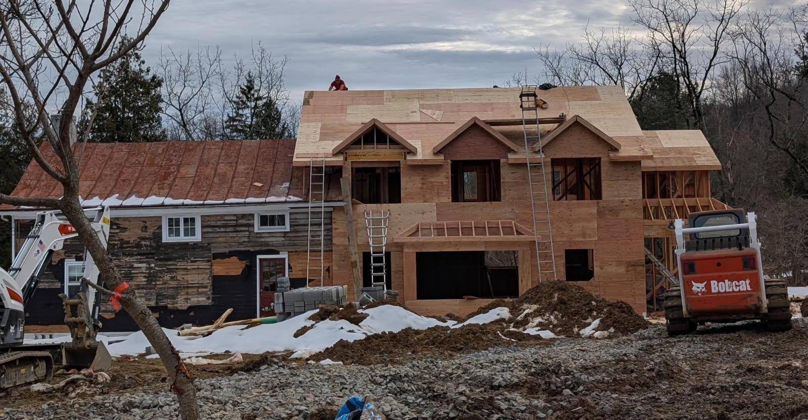 Custom home under construction, sheathed with gabled dormers, beside an existing home